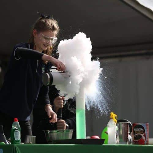 A woman pouring liquid nitrogen into a measuring cylinder with bubbles pouring out in the sunlight