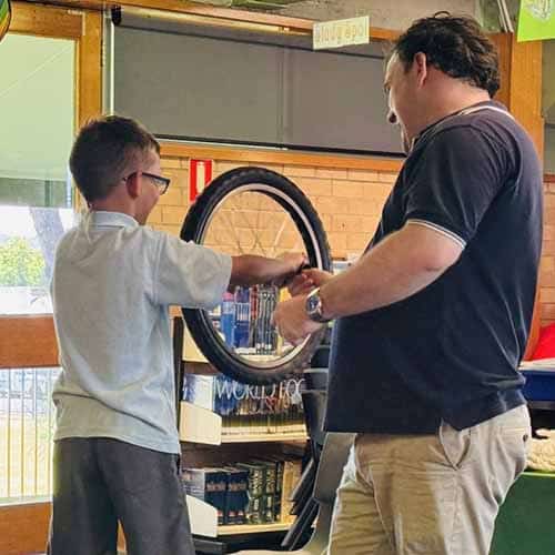 A student holding a bike wheel by its handles while a science presenter helps him spin
