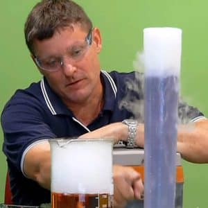 A man pointing at bubbling dry ice beaker and measuring cylinder with coloured liquids inside