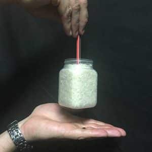 A bottle of rice being held up by a pencil that has been pushed into it.