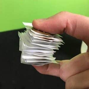 A stack of coins with paper inbetween them being held between a thumb and forefinger