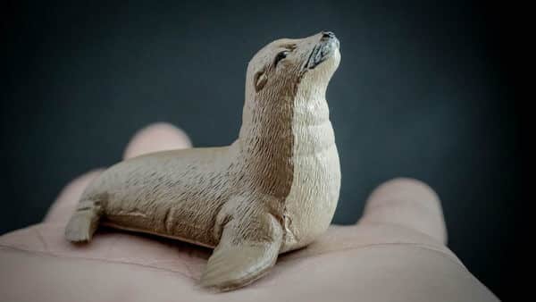 Person holding up a replica of a Sea lion in the palm of their hands. Front view