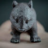 Person holding in the palm of their hand a replica of a common wombat. Front view