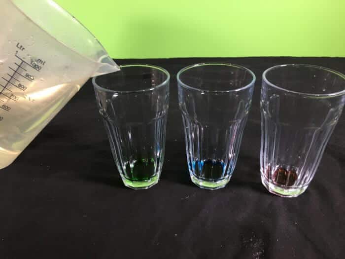 Making rock candy science experiment - adding hot water to food colour in glasses