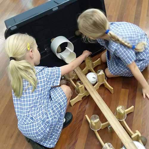 Two students setting up a wooden ramp with balls and pipes