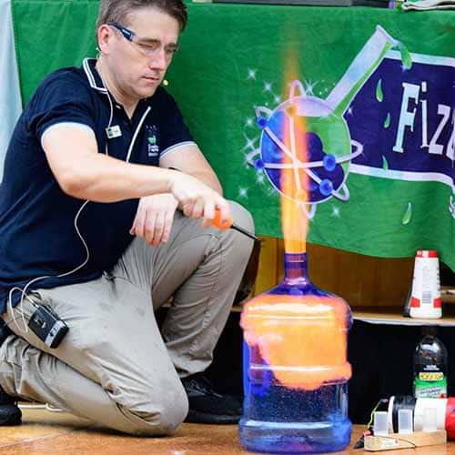 A science presenter lighting a fire inside a giant water bottle