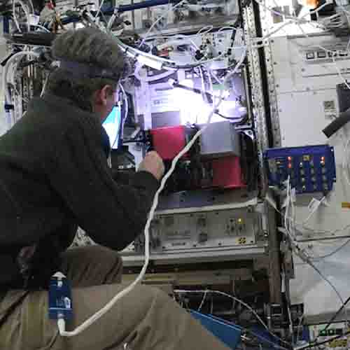 An image of an astronaut using ExoLab on the International Space Station. There are wires and technical equipment surrounding this person