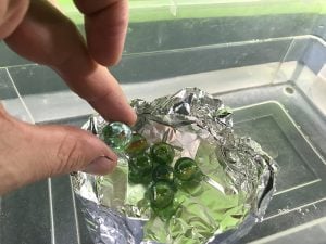 Foil boat floating on water while a guy adds marbles on top