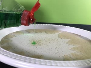 Adding detergent to a plastic bowl of water and pepper.