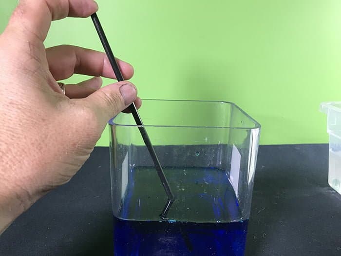 Blue water getting extracted from a Blue jug of water by a piece of straw.