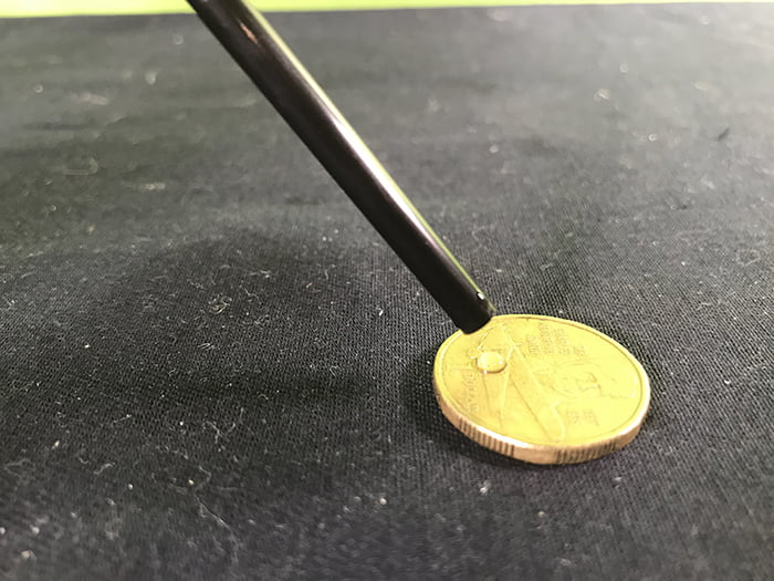 Water dropping out of a pipette onto a coin, one tiny drop of water