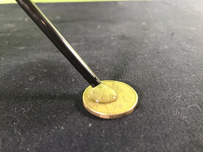 Water dropping out of a pipette onto a coin, one big drop of water