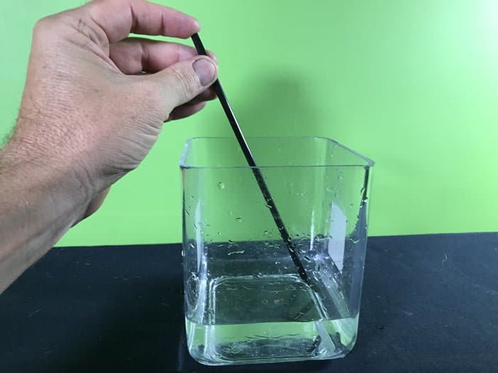 Person with a straw trapping water out of a jar of water into a straw.