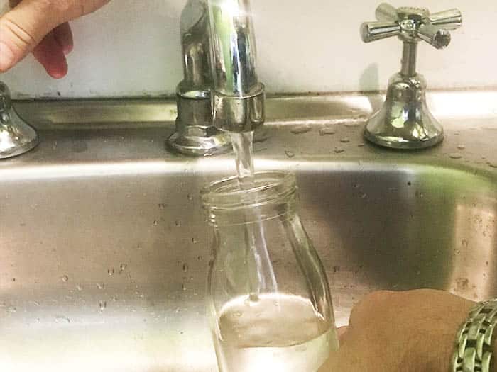 A glass bottle underneath a tap collecting hot water