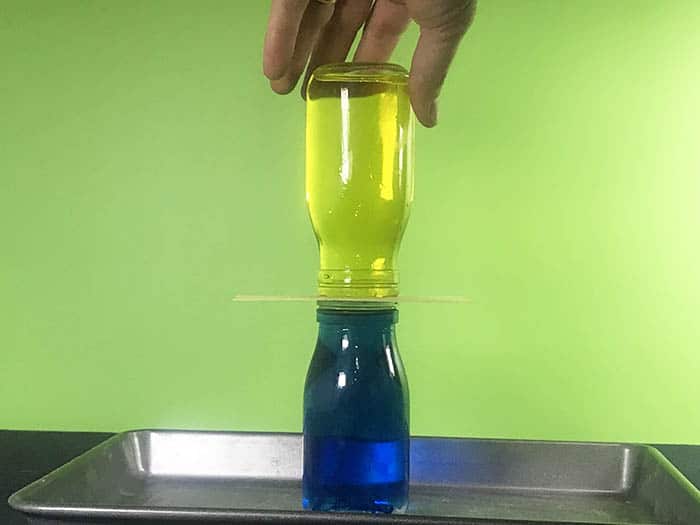A yellow bottle of water upside down above a blue bottle of water with an index card in-between them.
