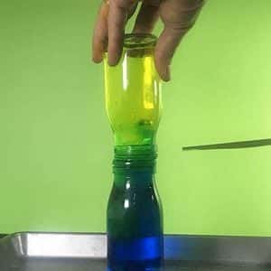 Yellow water moving downwards and blue water moving upwards between two glass bottles connected together