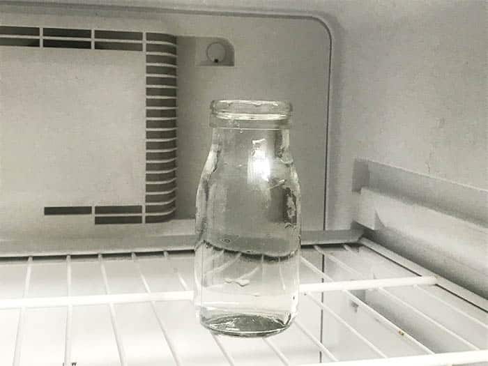 A glass bottle filled with water in a freezer