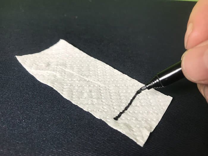 Drawing a black line using a felt tip marker across the bottom of a white paper toweling strip