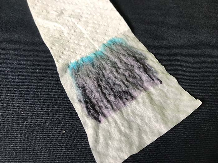 Spread out black ink on whote paper, showing a thin blue line on one edge of the black ink streak