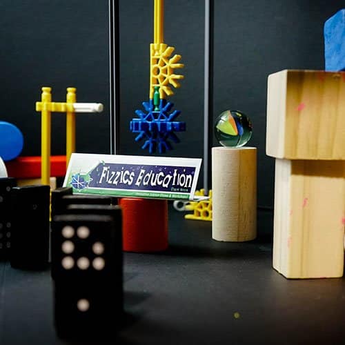 An assortment of wooden blocks, coloured plastic gears, dominoes and marbles arranged on a table with a black table cloth