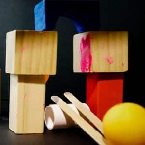 Two paddle pop sticks on a cut PVC pipe with stacked blocks and a ping pong ball