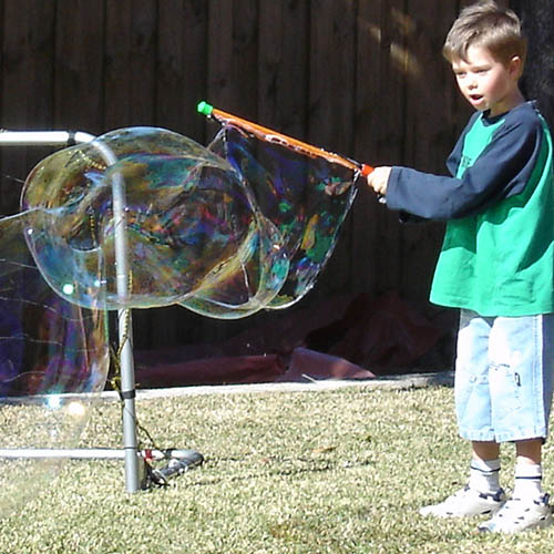 young boy making giant bubbles whilst having a surprised face