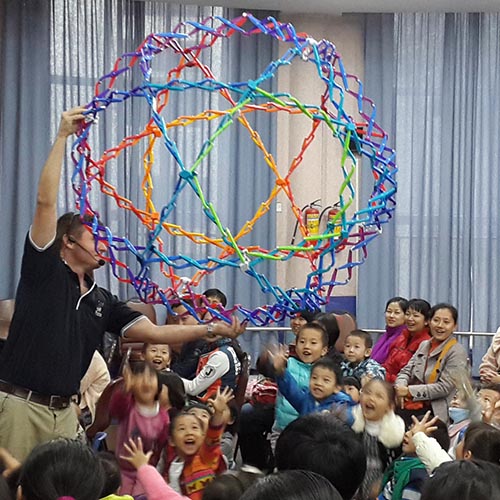 A man holding a mega hoberman sphere over very happy preschoolers during a science show