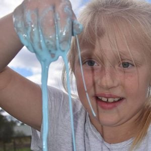 A blonde girl smiling and watching blue slime dripping out of her hand in front of her
