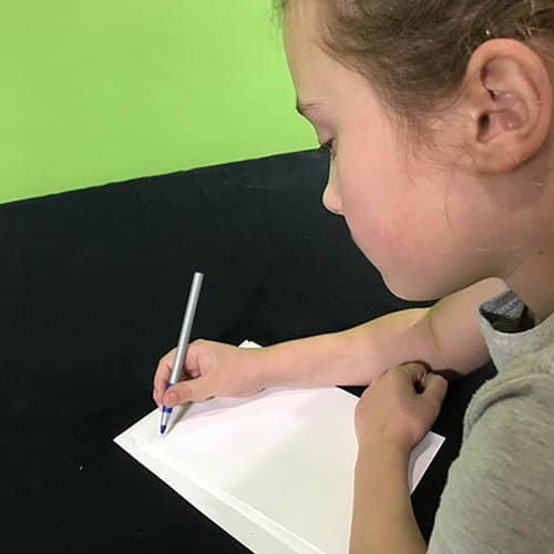 Student using a pen to write on paper on a black table cloth