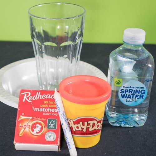 Matches, a candle, play dough, a water bottle a glass and a plate on a desk