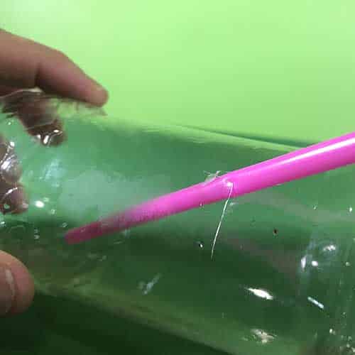 A pink straw pushed through the side of plastic bottle