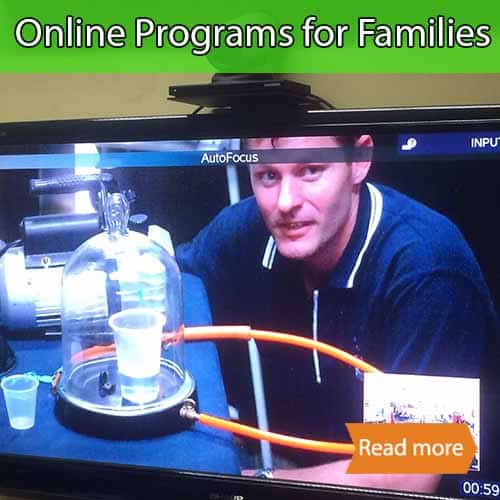 A picture showing a man on a TV using a bell jar and vacuum pump. There is a plastic cup with water inside the bell jar. There is a tandberg camera on top of the tv