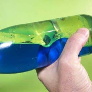 A hand holding a bottle which contains oil and blue coloured water. There is a wave moving through the bottle