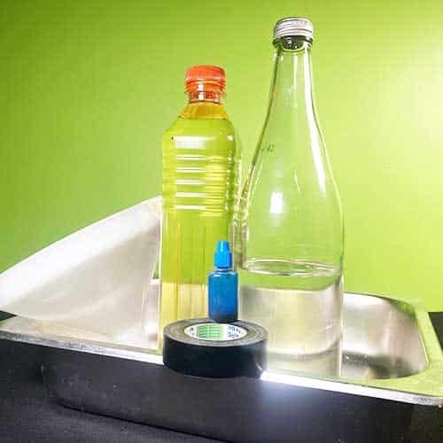 A metal tray with a glass bottle, black insulation taoe, blue food colouring, vegetable oil and a white funnel