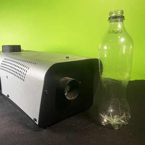 A fog machine next to a plastic soft drink bottle on a desk