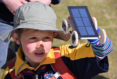 A scout holding a solar car toy up to the Sun
