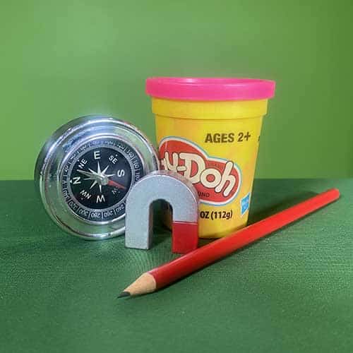 A compass, play dough, sharp pencil and horseshoe magnet on a green table