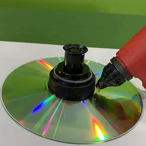 A hot glue gun being used to secure a pop-top sports drink bottle lid onto a CD
