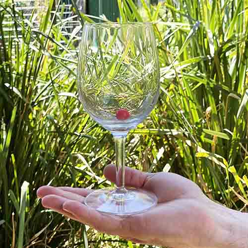 A hand holding a wine glass with a small red ball inside