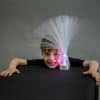 A child next to a fibre optic lamp. It shows purple light shining through many optic fibres with a grey background