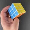 A magic cube held in the hand showing three sides of the cube (blue, yellow ad orange)
