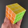 A magic cube held in the hand showing three sides of the cube (orange, yellow and green)