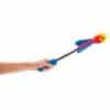 A hand using a long handle to throw a flick n fly rocket. The flick n fly rocket is coloured with red flames on a yellow background. The tail of the rocket is blue