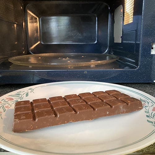 A chocolate bar on a white plate next to microwave