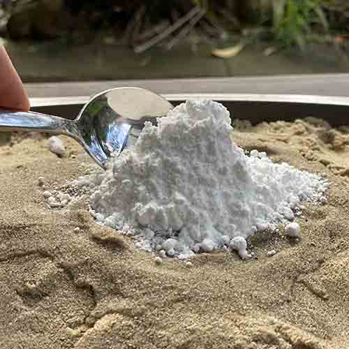 A metal spoon creating a pile of white powder on sand