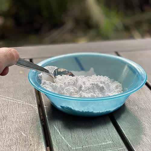 A hand mixing white powder with a metal spoon in a blue bowl