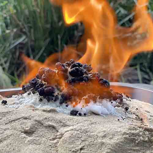 A pile of white powder on sand with the top of it burning