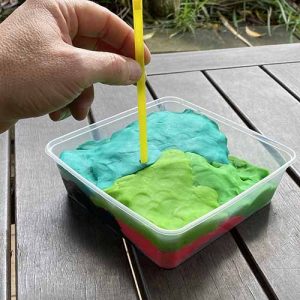 A hand pushing a yellow straw into a tray of play dough