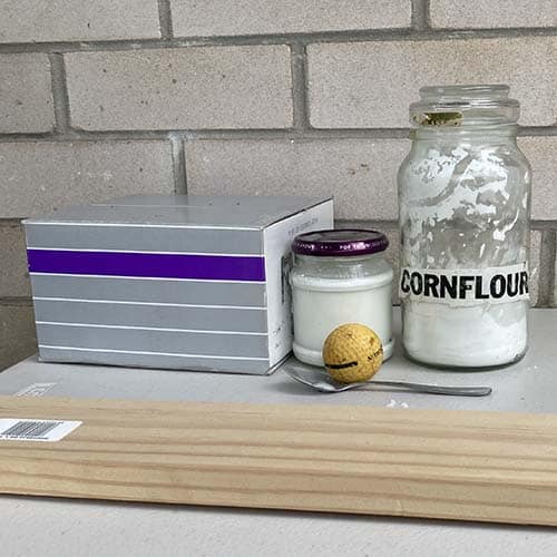 A box, wooden plank, cornflour, yellow golf ball, spoon and jar of corn flour