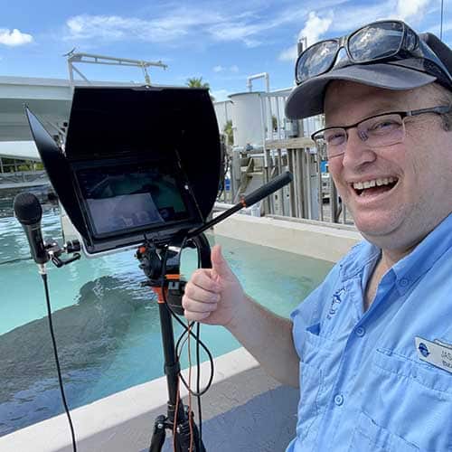 Jason with a an ipad on a stand with a microphone in front of a manatee pool